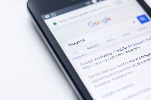 A smartphone screen displays a Google search for “analytics,” highlighting results and tabs for All, Images, News, and Apps—valuable tools when exploring SEO strategies for small businesses. - Clio Websites | Top Canadian Web Design Company