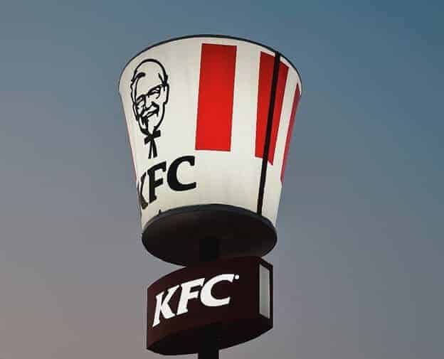A large, illuminated KFC bucket sign with red and white stripes and the KFC logo stands against a clear sky—showing how bold images like these can help increase your website conversion rate. A smaller rectangular KFC sign sits just below it. - Clio Websites | Top Canadian Web Design Company