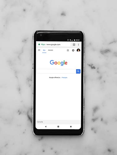 A smartphone lying on a white marble surface displays the Google homepage, highlighting the importance of SEO plugins for WordPress to boost your site's visibility in search results. - Clio Websites | Top Canadian Web Design Company