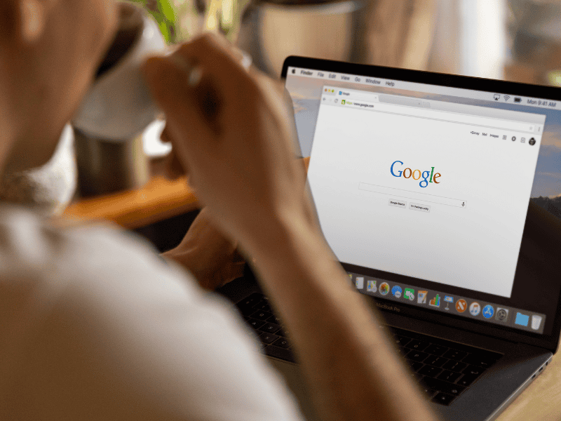 A person holds a cup while sitting at a desk and using a laptop that displays the Google homepage, perhaps searching for Calgary SEO services. - Clio Websites | Top Canadian Web Design Company