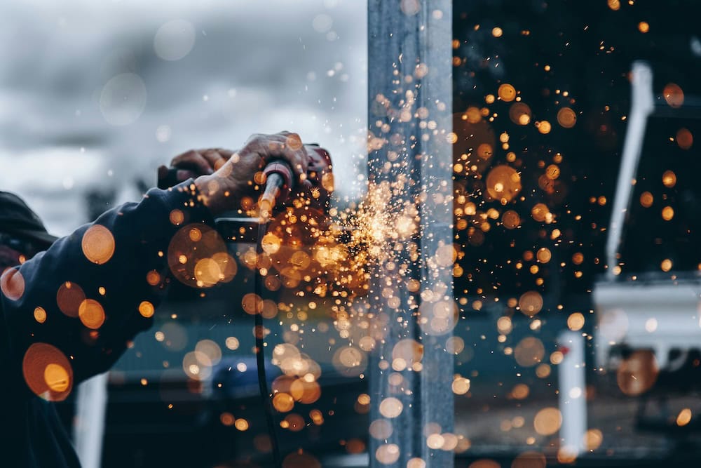A person uses a power tool to cut or grind metal, creating bright orange sparks that scatter in the foreground. The blurred background highlights the intense shower of sparks, evoking the dynamic energy of manufacturing web design. - Clio Websites | Manufacturing Web Design Company