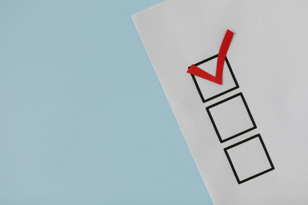 A close-up of a paper with three checkboxes, the top box marked with a large red checkmark, illustrating website optimization services, and a light blue background on the left side. - Clio Websites | Top Canadian Web Design Company