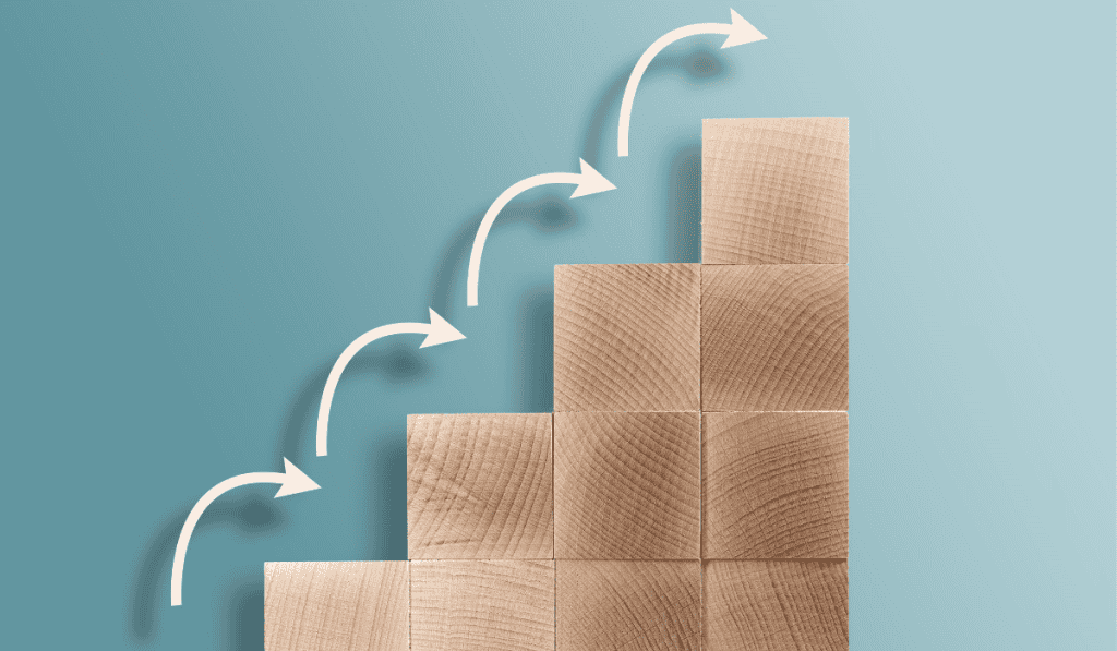 Four stacks of wooden blocks form steps on a blue background, with white arrows curving upward from one step to the next, symbolizing progress or growth—much like building a successful WordPress website for small business Calgary. - Clio Websites | Top Canadian Web Design Company
