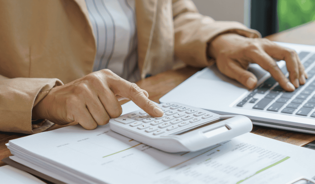 A person uses a calculator and types on a laptop, with financial documents on a wooden desk, suggesting they are managing accounting tasks or budget calculations for a WordPress website for nonprofits in Calgary. - Clio Websites | Top Canadian Web Design Company